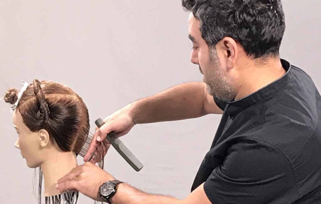 Male hairstylist using left handed scissors to cut hair on mannequin head