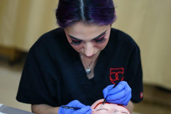 Woman applying eyelash extensions on mannequin.